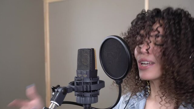 A fashionable energetic singer sings into a microphone in a recording studio