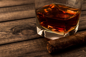 Glass of brandy and cuban cigar on an old wooden table. Close up view, focus on the cuban cigar