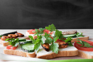 Sandwiches with seafood, vegetables and herbs, on a wooden table top and a black background, close up