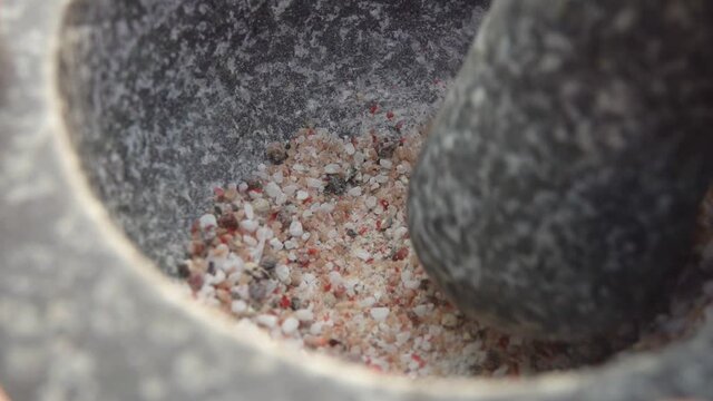Heavy pestle is grinding a mix of spices, peppers and sea salt in the mortar