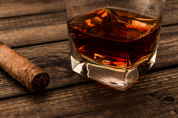 Glass of brandy and cuban cigar on an old wooden table. Close up view