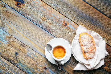 Cup of espresso coffee and brioche on an old wooden table.