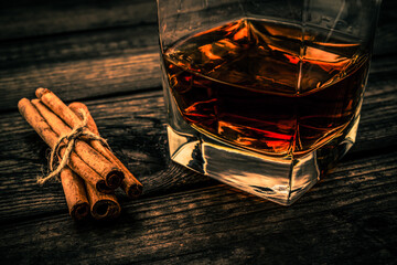 Glass of brandy with cinnamon sticks tied with jute rope on an old wooden table. Close up view