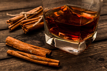 Glass of brandy with cinnamon sticks tied with jute rope on an old wooden table. Close up view
