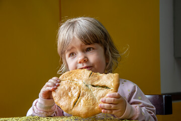 Portrait of a little girl eating a large pizza indoors on a neutral background. Concept: a snack while traveling, exotic local dishes.