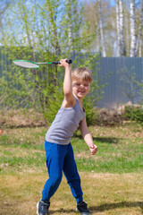 A fair-haired child plays badbinton on the lawn.