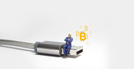 Businessman figure sitting on usb USB type C cable. Bitcoin cryptocurrency concept.