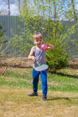 A fair-haired child plays badbinton on the lawn.