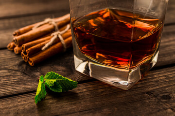 Glass of brandy with mint sprig and cinnamon sticks tied with jute rope on an old wooden table....