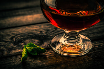 Glass of brandy with mint sprig on an old wooden table. Close up view, shallow depth of field, focus on the mint sprig