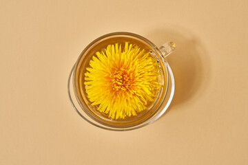 A cup of dandelion tea with dandelion flowers on pastel beige background