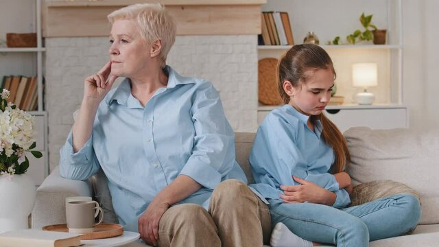 Upset old grandmother and unhappy offended granddaughter sit on sofa not talking having two generation gap family conflict concept, elderly grandparent little grandchild quarrel misunderstandings