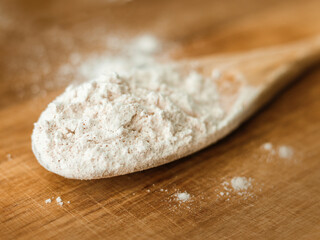 Fototapeta na wymiar wooden spoon in macro shot on wood cutting board with flour in kitchen
