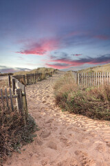 Path to the beach through the dunes surrounded by a wood fence at the sunset. Sky with amazing colors.