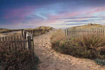 Path to the beach through the dunes surrounded by a wood fence at the sunset. Sky with amazing colors.