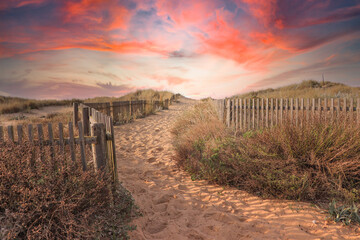 Path to the beach through the dunes surrounded by a wood fence at the sunset. Sky with amazing colors.