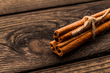 Three cinnamon sticks tied with jute rope on an old wooden table. Close up view