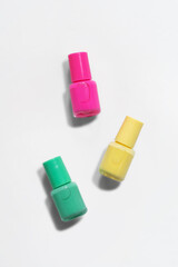 A collection of colored nail polishes on a white background, with hard shadows. Creative mockup of isolated cosmetic bottle with yellow, green and pink nail polish. Top view. Flat lay. Vertical