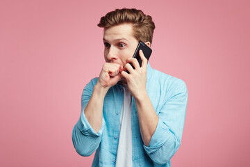 Nervous male keeps fists in mouth during conversation via smartphone