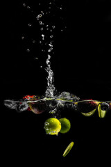 bright juicy fruits with splashes fly into the aquarium on a black background