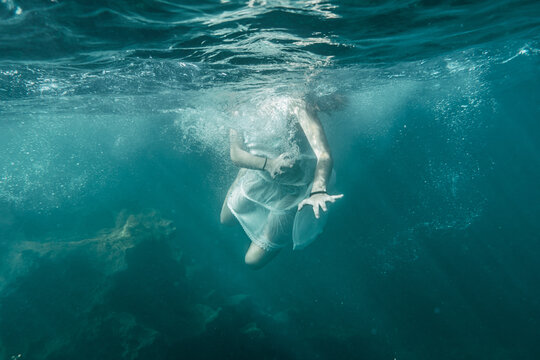 Image of a young woman with a white dress diving into the sea, underwater image, summer lifestyle of a young Caucasian brunette