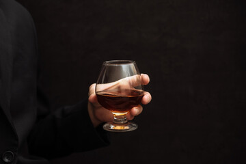 Naklejka na ściany i meble whiskey in a glass on a black background copy space. a man holds in his hand an alcoholic drink scotch, brown cognac. the concept of alcoholic drink, alcoholism