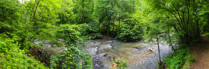  a stunning panoramic shot of the rushing river water of Big Creek river with lush green trees and large rocks on the banks and in the middle of the river at Vickery Creek in Roswell Georgia