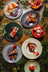 Variety of restaurant style deserts on a wooden table decorated with plants, michelin star food.