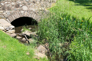 Obraz premium formal garden setting with stone arch bridge culvert over a small river creek with lush greenery