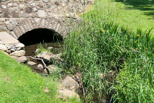 formal garden setting with stone arch bridge culvert over a small river creek with lush greenery