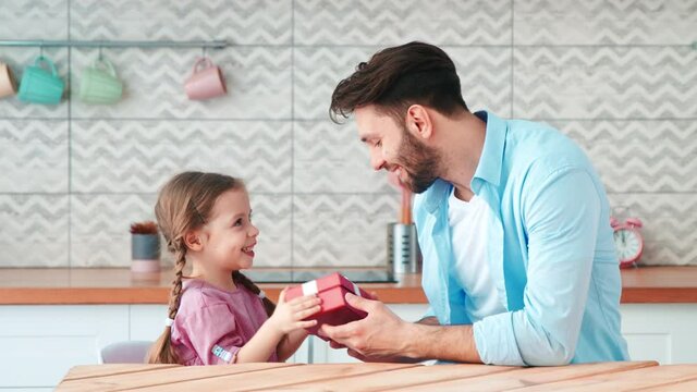 A young single dad giving a present to his little daughter. Father giving a birthday present to his daughter.