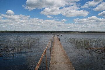 Long iron bridge on a wide river, blue sky with white clouds, old pier on the Dnieper river
