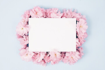 Blank paper and cute pink flowers on blue background