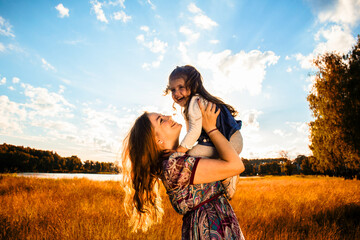 happy mother with a little daughter, having fun in nature, in the rays of the sunset - 434616086