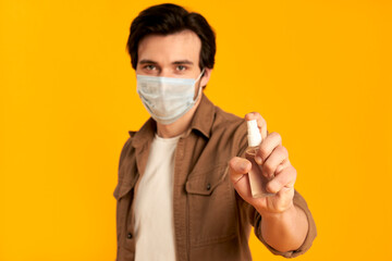 Young bearded man in protective medical mask with sanitizer isolated on orange background. Disinfection, hand hygiene. Life in the quarantine of COVID-19 coronavirus infection.