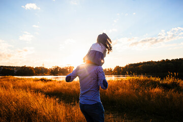 happy father with a little daughter, having fun in nature, in the rays of the sunset