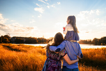 happy family with a little daughter in a field in nature, looking forward, view from the back, in the rays of the sunset