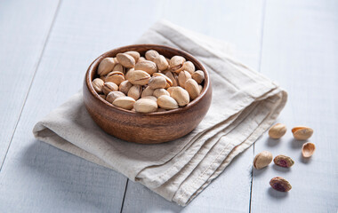 Pistachio nuts in a brown bowl on a napkin and  white wooden background. Top view and copy space