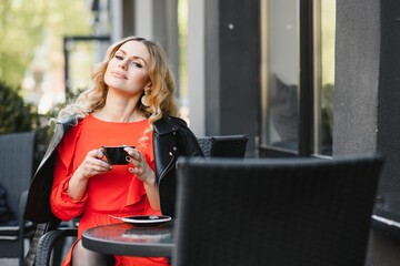 young woman drinks coffee in street cafe. Lady with beautiful makeup in expensive blouse is mysteriously.