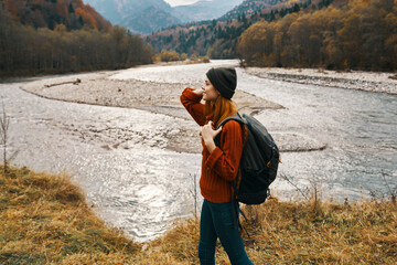 woman traveler with backpack on the river bank in the mountains side view