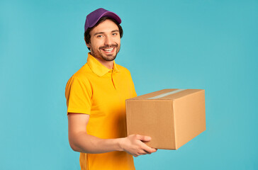 Young bearded courier delivery man in uniform holds a box isolated on blue background. Home...