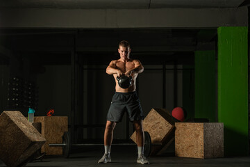 Naklejka premium Full-length photo of a handsome man with a naked torso exercising with a kettlebell on a dark background