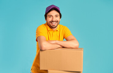 Young bearded courier delivery man in uniform with boxes isolated on blue background. Home delivery.