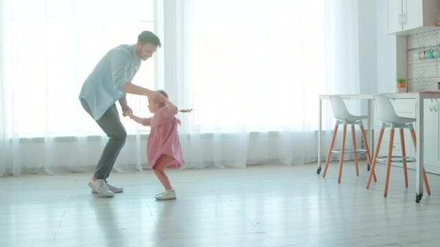Happy young father and little preschool girl dancing at home.