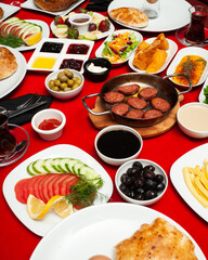 Turkish breakfast table. Frying pan with fried sujuk, buns, bread, sauces, olives, salad, tea, vegetables on a festive red tablecloth