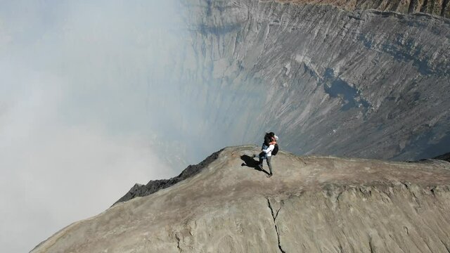 Aerial view of couple embracing on ridge of Mount Bromo volcano (Gunung Bromo) in East Java, Indonesia. Happy woman waving to camera. Mount Bromo is active volcano. Concept of adventure and travelling