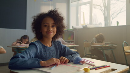 African girl sitting at desk in classroom. Smiling student posing at camera