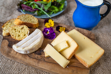 2 sorts of cheese, flower, bread on wooden kitchen board, green salad and blue pitcher.