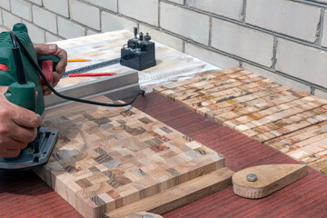 A carpenter with a hand-held electric milling cutter makes an end cutting board.