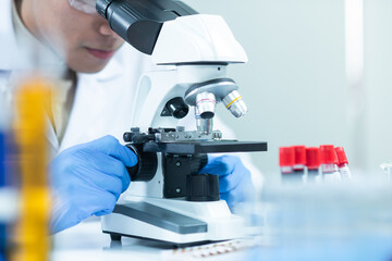 Young asian scientist man looking through a microscope in a laboratory. To check the blood sample in the sampling tube placed on the desk